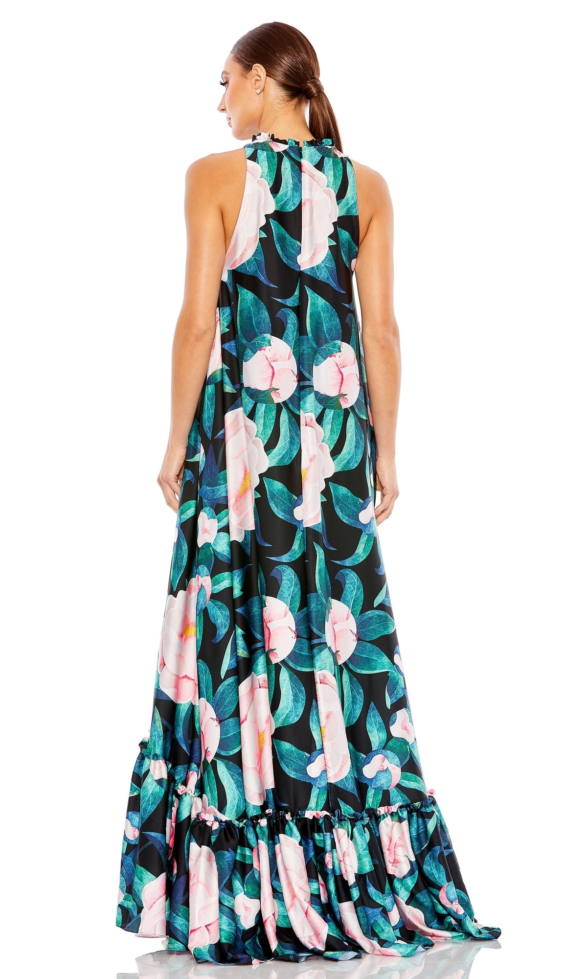 A woman faces away in the Mac Duggal 11406 floral-print long formal dress, featuring bold pink and white flowers with green leaves on a dark background and finished with a flowing, ruffled hem.